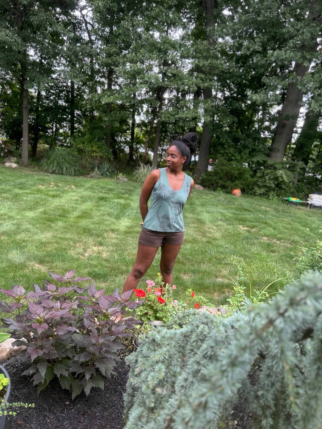 Model wearing the Slide Eagles sleeveless football graphic tank with brown shorts in a garden, full-body lifestyle view.
