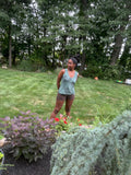 Model wearing the Slide Eagles sleeveless football graphic tank with brown shorts in a garden, full-body lifestyle view.